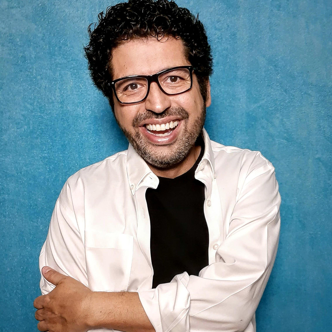 Portrait of Juan smiling at the camera in front of a blue background