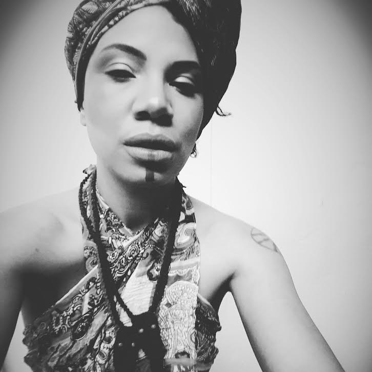 Robin Akimbo is photographed in an Afro-Caribbean wrap, dress and jewelry in a black-and-white close-up.