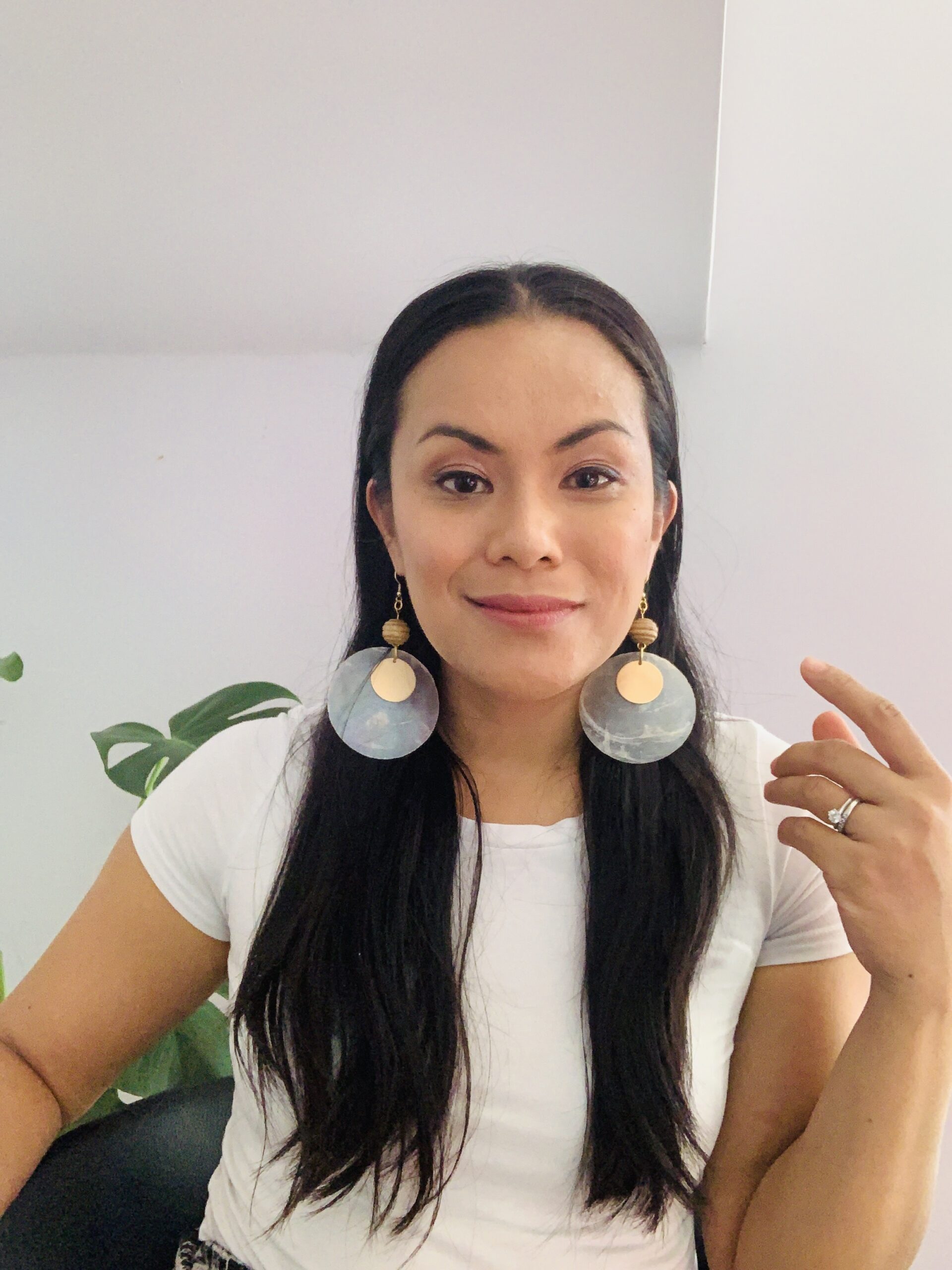 Blessyl Buan is smiling at the camera, wearing a white t-shirt and her long brown hair and large circular earrings framing her face.