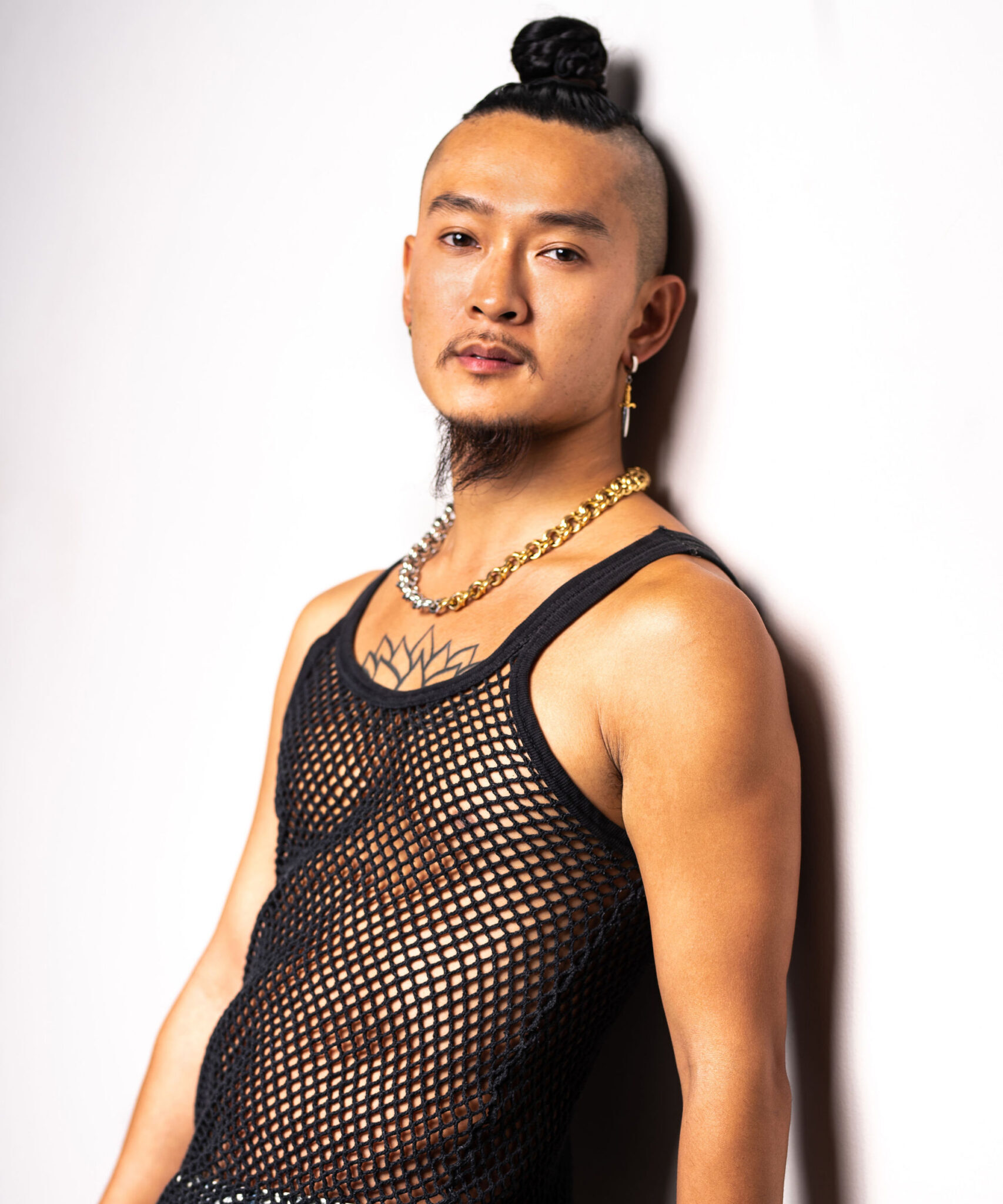 Headshot of Pilot Episode Choreographer Sze-Yang Ade-Lam, east asian male in man bun and mesh tank posing on the wall