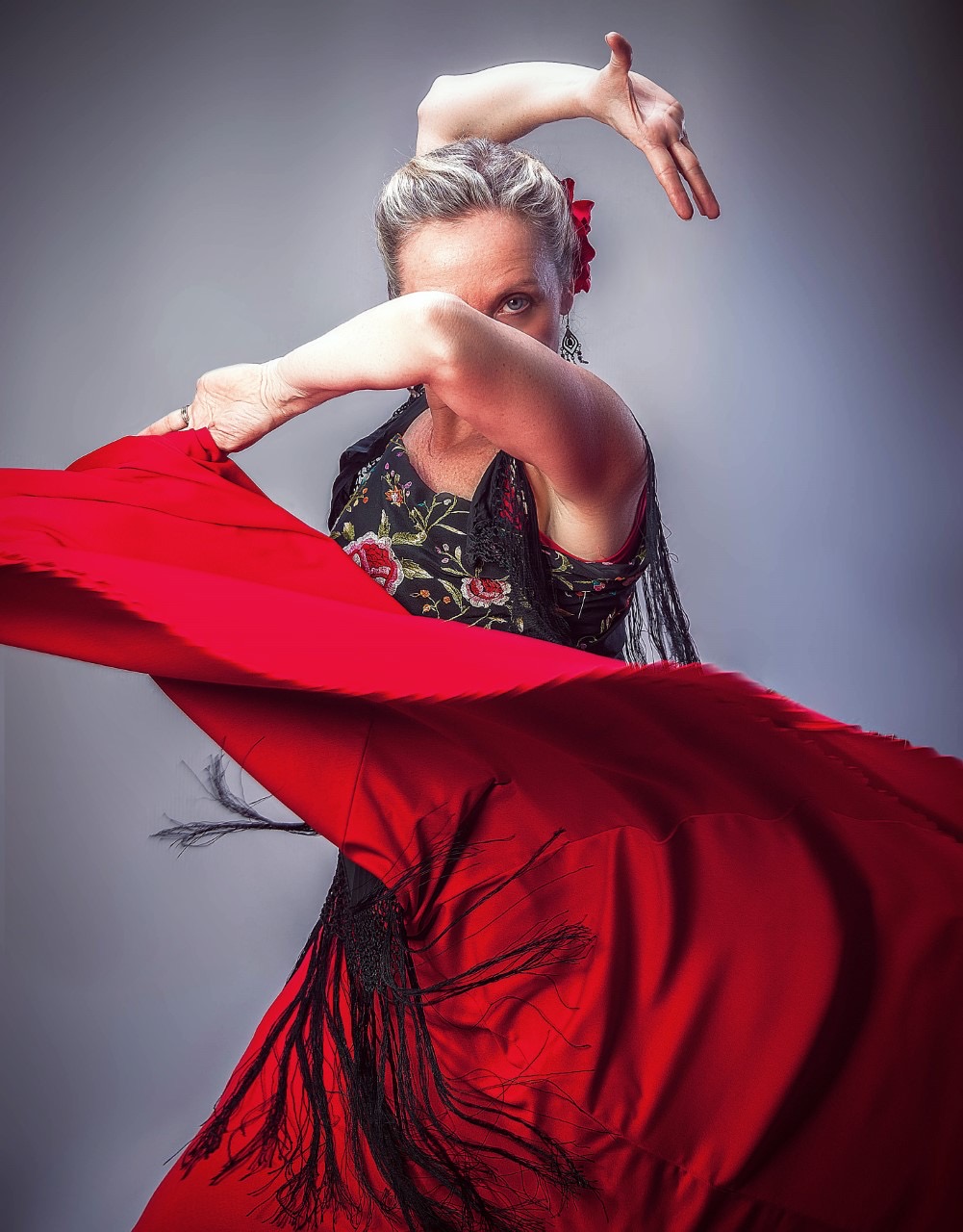 Dancer poses for headshot as she swings her dress over her face with arms in motion.