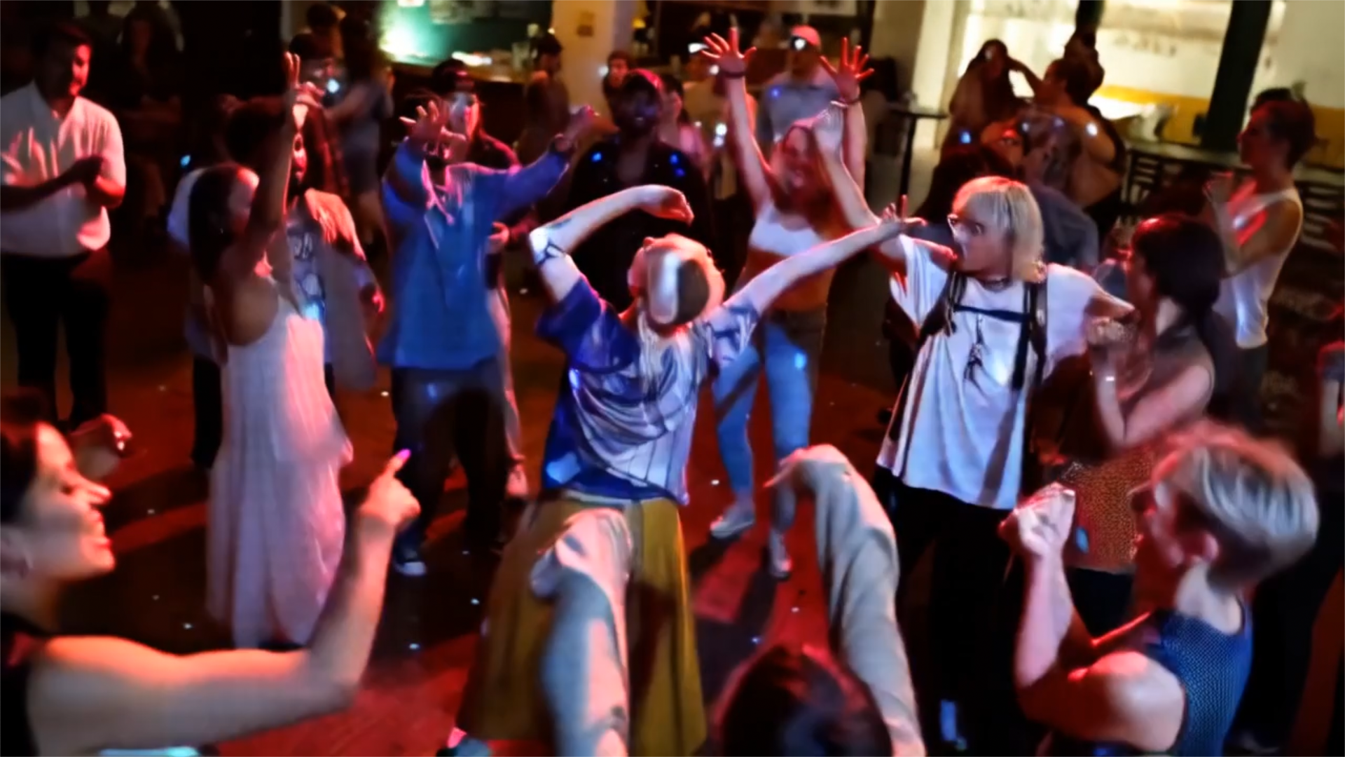A lively dance floor scene featuring diverse people energetically dancing under colorful lights, creating a festive atmosphere.